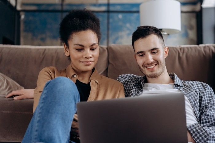 Two people on a couch smiling looking at a laptop
