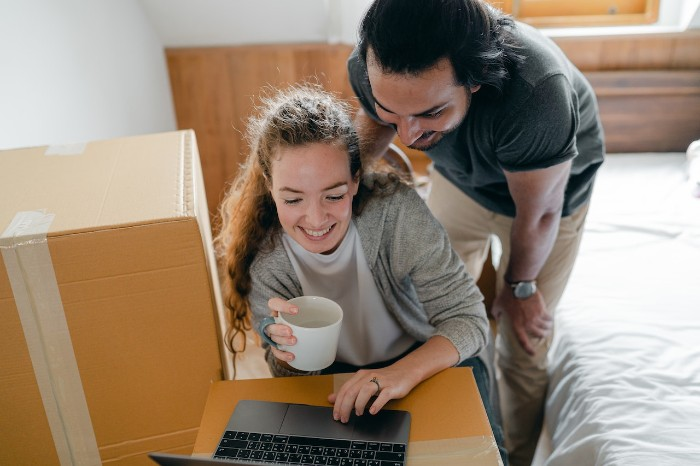 Two joyful persons looking at a computer in a bedroom with moving box.